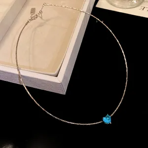 Detail shot of a minimalist silver-tone necklace with a bright blue heart pendant.