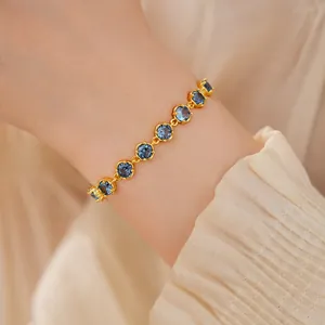 Close-up of 18k gold plated bracelet with sparkling round blue zirconia stones on wrist.