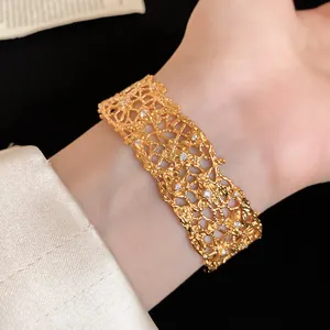 Close-up of a gold-plated lace-textured open bangle with sparkling stones on a wrist.