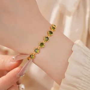 Detailed view of an 18k gold-plated bracelet with green round zircon stones on a wrist