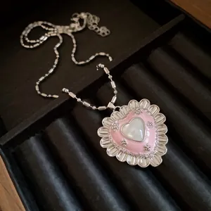 Detail of vintage heart pendant with pink enamel and cat-eye stone on black velvet tray.