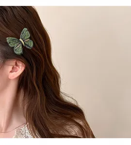 Detailed close-up of a green embroidered butterfly hair clip worn on wavy long brown hair.