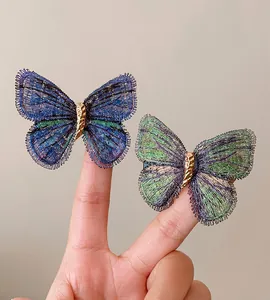 Detailed view of two elegant embroidered butterfly hair clips in blue and green hues.