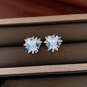 Dettaglio di orecchini a lobo in argento a forma di fiore con zirconi blu chiaro.