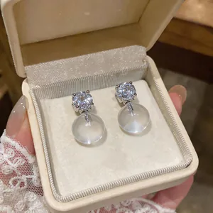 Close-up of French style silver needle earrings with clear resin round studs and diamonds