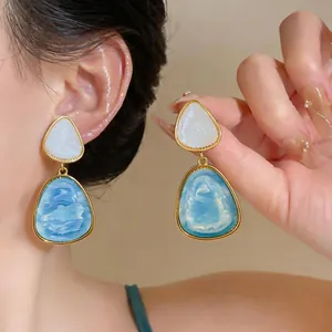 Primo piano di eleganti orecchini in resina marmorizzata blu e bianca con oro retro