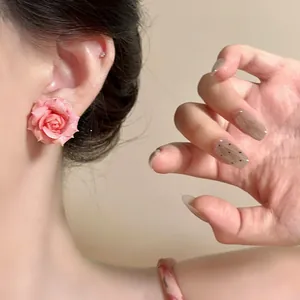 Detail shot of a gradient pink rose stud earring worn on an ear, elegant floral design