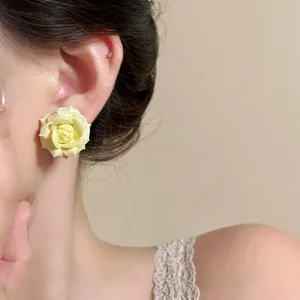 Close-up of a delicate yellow rose stud earring on a model's ear with soft lighting