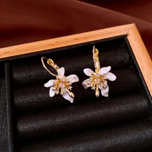 Élégantes boucles d'oreilles fleur blanche avec finition dorée et zircons brillants