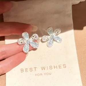 Macro view of sparkling light blue glass flower stud earrings resting on a beige gift pouch
