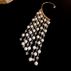 Detailed macro shot of an elegant pearl and crystal tassel ear cuff on black background