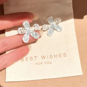 Detailed view of silver flower stud earrings with sparkling crystals on a gift bag