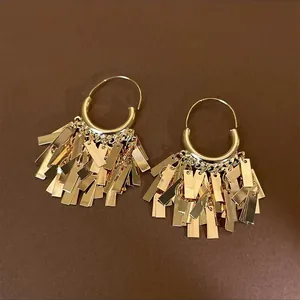 Detailed macro view of gold sequined tassel hoop earrings on brown background