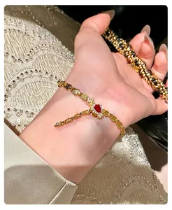 Detailed view of a gold snake-link bracelet featuring a red gemstone on a wrist.