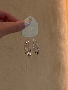 Detail view of minimalist silver earrings with shimmering sequin tassels on display card.