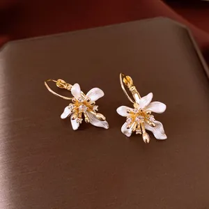 Détail de boucles d'oreilles fleurs en zircone avec des pétales en émail blanc.