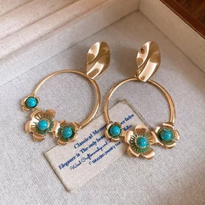 Elegante goldene Creolen mit Blumen und Türkissteinen in einer edlen Schmuckschatulle.