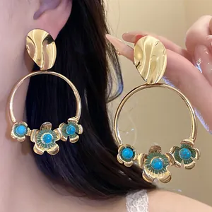 Detailansicht großer goldener Creolen mit blauen türkisfarbenen Blumenanhängern