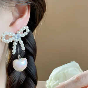 Detailed close-up showing the elegant bow and heart-shaped pearl drop earrings worn on ear