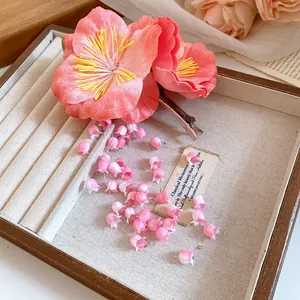 Close-up of a pink fabric flower hair clip with lily-of-the-valley tassels on a tray
