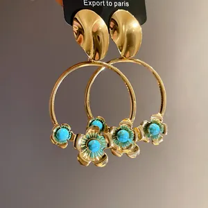 Nahaufnahme von vergoldeten Creolen mit eleganten türkisfarbenen Blumenanhängern.