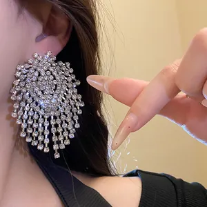 Detail view of oversized sparkly rhinestone geometric tassel earrings on a model