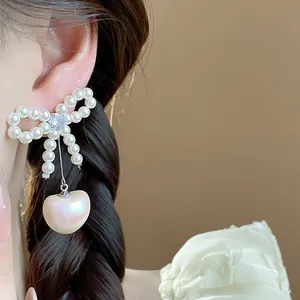 Close-up detail of elegant bow-knot and heart pearl drop earrings worn by model