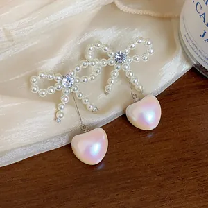Detail of bow earrings with zircon center and iridescent heart-shaped pearl drop