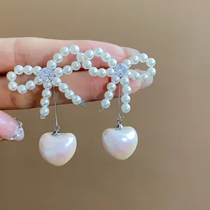 Close-up of elegant pearl bow earrings with a heart-shaped pearl drop and zircon.