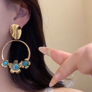 Detailaufnahme goldener Creolen mit Blumenanhängern und türkisfarbenen Perlen am Ohr.
