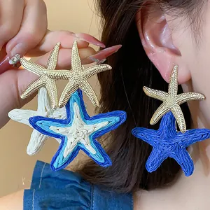 Detailed macro shot showing textured blue and gold starfish drop earrings on ear