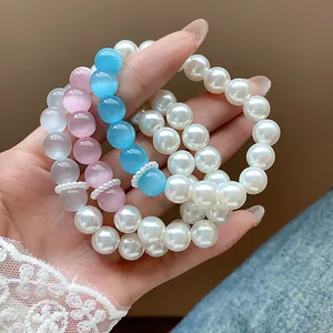 Close-up detail of elegant pearl and colorful cat-eye stone bead bracelets on hand.