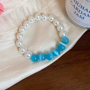 Detailed view of pearl and blue cat-eye stone bracelet on cream silk background