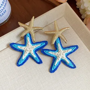 Detail view of colorful woven raffia starfish earrings with golden starfish studs