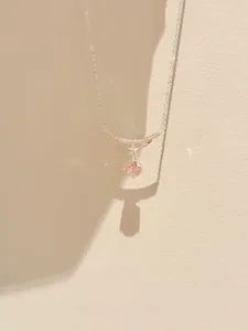 Close-up detail of a sparkling zircon flower pendant on a minimalist silver collar chain.