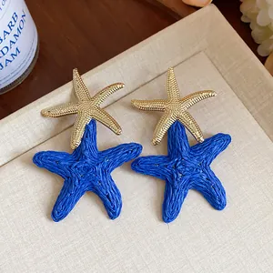 Close-up detail of blue raffia woven starfish and gold metal stud earrings for summer resort