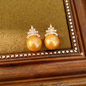 Vue détaillée d'élégantes boucles d'oreilles perles dorées avec couronne en zircone.