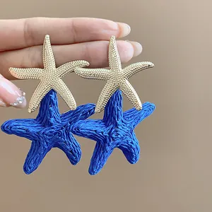 Detailed view of blue raffia woven starfish earrings with golden metallic accents.