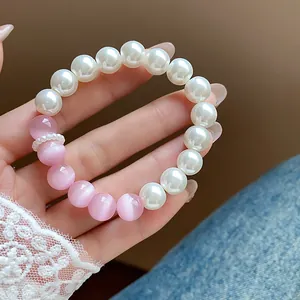 Close-up of elegant bracelet with white pearls and pink cat's eye beads held by hand