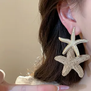 Detail of double layer starfish earrings featuring gold-tone metal and woven raffia design.