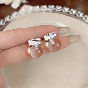 Close-up detail of minimalist silver stud earrings with clear resin spheres