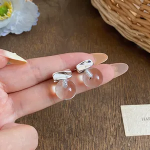 Close-up detail showing minimalist silver stud earrings with clear round resin spheres