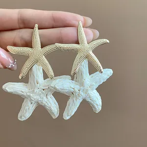 Detail of gold textured and white raffia woven starfish earrings for a holiday look