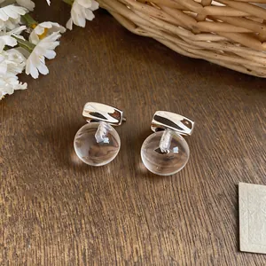 Macro view of minimalist silver earrings with transparent resin balls on wooden surface