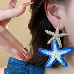 Close-up of stylish blue raffia and gold starfish earrings worn by a model for a vacation look