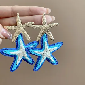 Close-up detail of handcrafted woven raffia starfish earrings with gold accents.