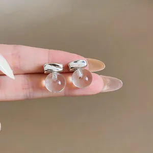 Close-up of minimalist silver needle stud earrings with clear round resin bead drops.