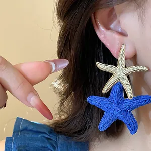 Close-up detail showing the gold metal and blue raffia textures of starfish earrings