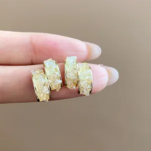 Close-up of elegant gold-plated hoop earrings with crushed crystal inlay on fingers