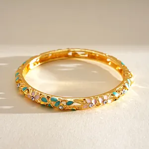 Nahaufnahme eines goldenen Retro-Armreifs mit bunten Emailleblumen und funkelnden Steinen